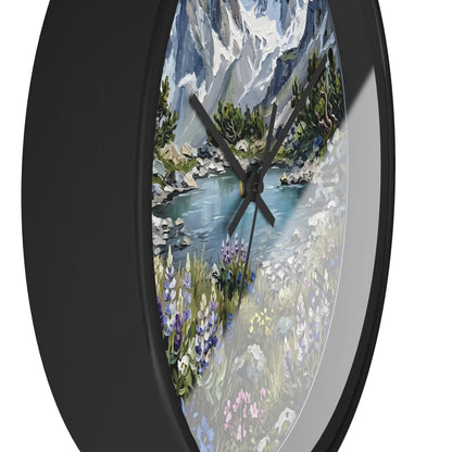 Round wall clock with a black frame and a scenic landscape print featuring mountains, a river, trees, and wildflowers, shown against a plain white background.
