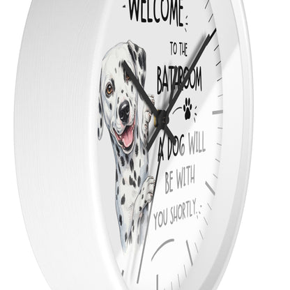 A white round wall clock with a printed illustration of a Dalmatian dog and the humorous text 'WELCOME TO THE BATHROOM A DOG WILL BE WITH YOU SHORTLY' on a clean white background.