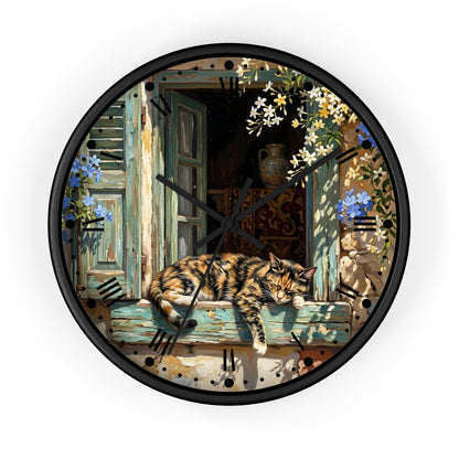 A round wall clock with a black frame and a detailed illustration of a tortoiseshell cat sleeping on a weathered blue window ledge, surrounded by flowers and shutters.