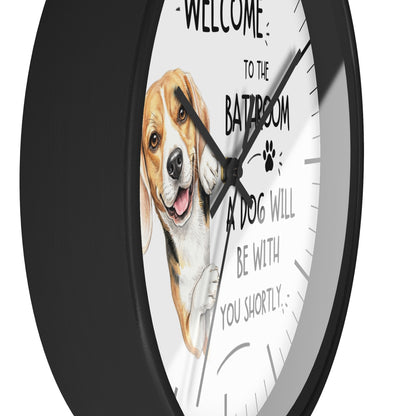 A round wall clock with a black frame and a white face featuring a painted beagle illustration and the text 'WELCOME TO THE BATHROOM A DOG WILL BE WITH YOU SHORTLY'.