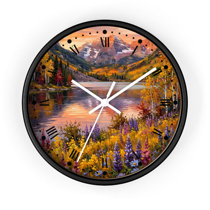 A round wall clock with a black frame and a scenic landscape print featuring a mountain lake, autumn trees, and wildflowers. The clock face has black Roman numerals and white hands, shown against a plain white background.