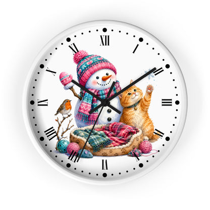 A round white wall clock with a colorful winter illustration on the face, featuring a snowman in a pink and blue knit hat, an orange tabby cat in a bed, a small bird, and holiday yarn and ornaments. The clock has black Roman numerals and black hands and is shown against a plain white background.