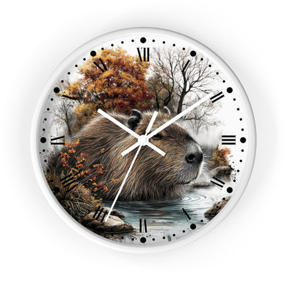 Round wall clock with a white frame and a printed nature scene featuring a capybara in a river with autumn trees in the background. The clock face has black Roman numerals, black dots for hours, and white clock hands.