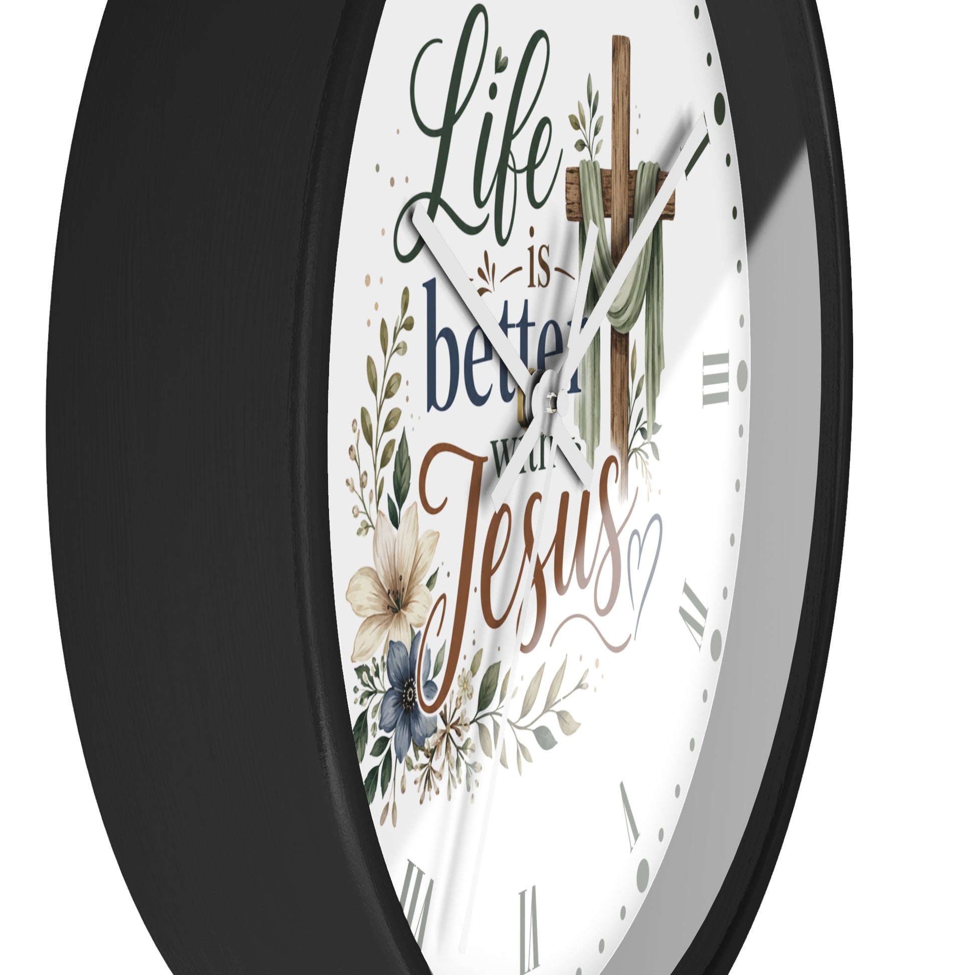 A close-up of a round wall clock with a black frame and a white face featuring the phrase 'Life is better with Jesus' in decorative script, along with floral illustrations and a wooden cross.