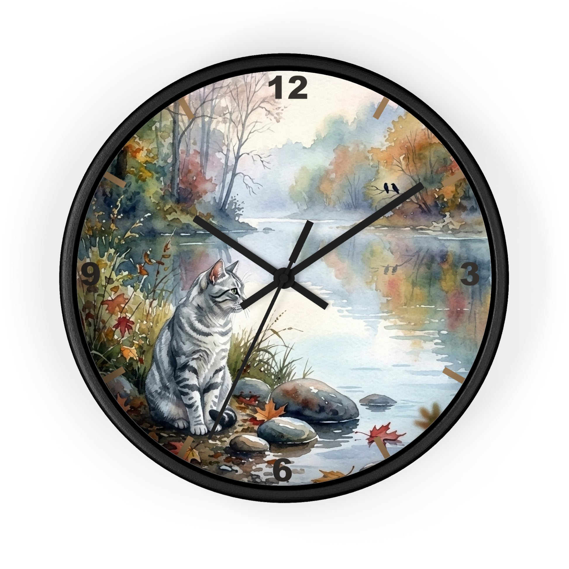 A round wall clock with a black frame and a printed scenic dial showing a gray tabby cat sitting by a calm river in autumn foliage. The clock has black numerals and black hands on a white background.