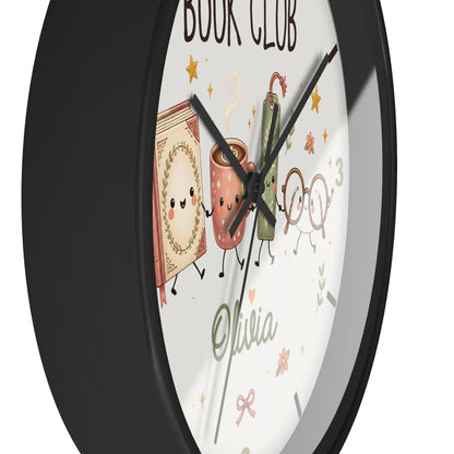 A round wall clock with a black frame and a white face featuring cute illustrated book and coffee cup characters, the words 'BOOK CLUB,' the name 'Olivia,' and decorative stars and leaves.
