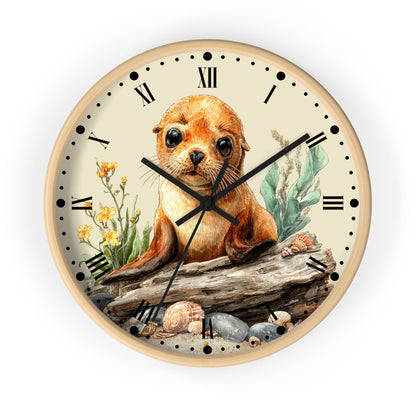 Round wall clock with a light wood frame and a cream dial, featuring a detailed illustration of a seal pup sitting on a log with seashells and sea plants. The clock has black Roman numerals, black hour and minute hands, and black minute markers.