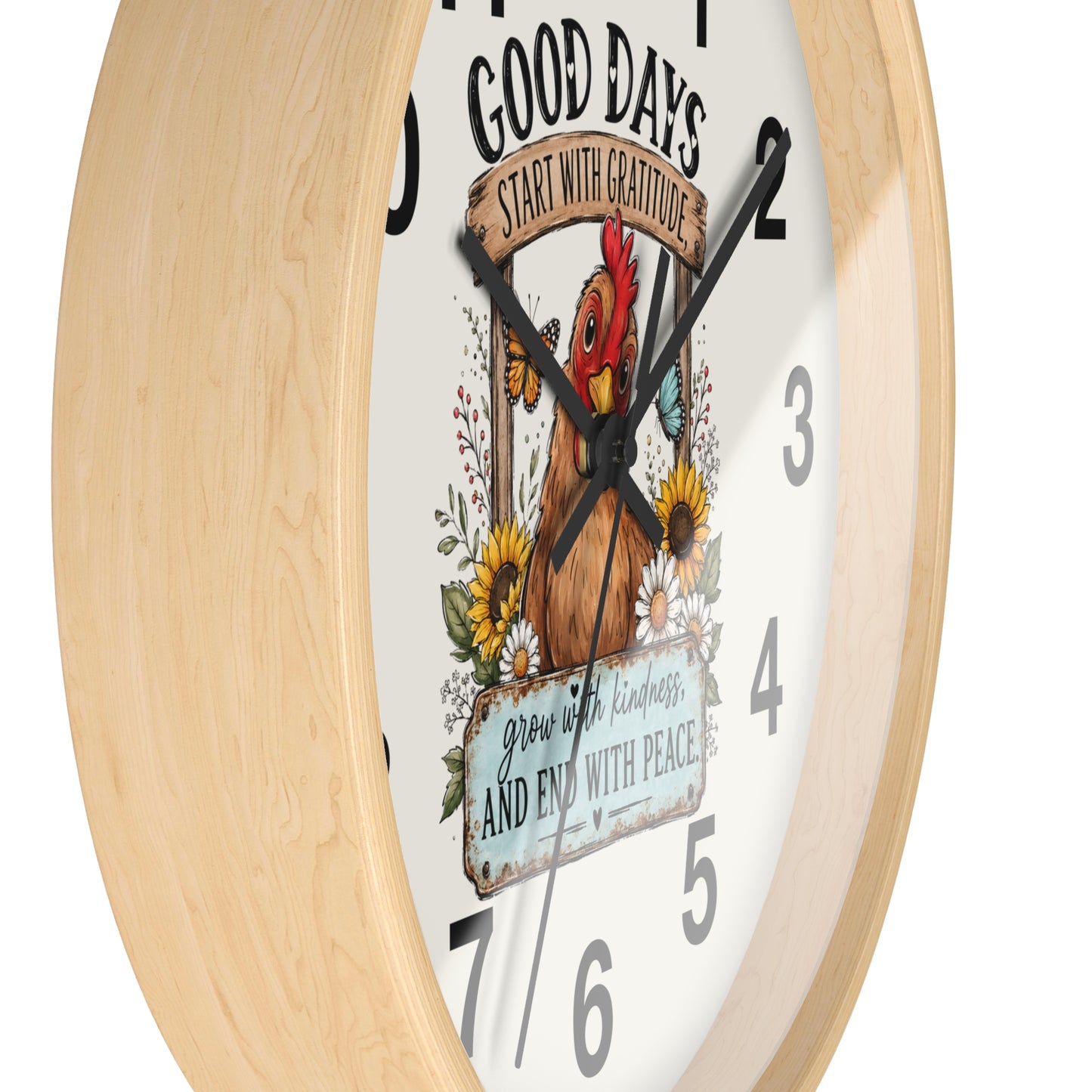 A close-up of a round wall clock with a light natural wood frame and a white face featuring a colorful rooster illustration, floral details, and inspirational text.