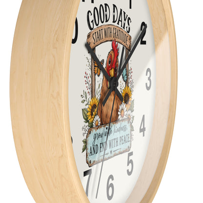 A close-up of a round wall clock with a light natural wood frame and a white face featuring a colorful rooster illustration, floral details, and inspirational text.