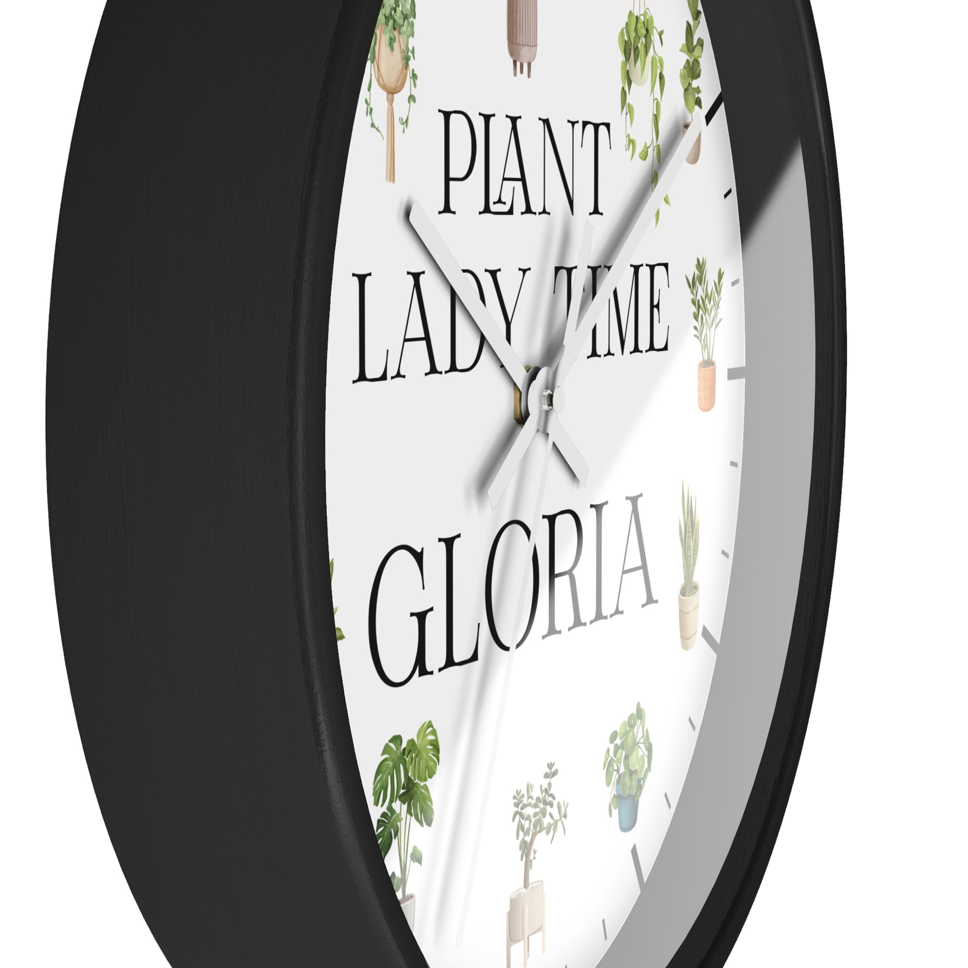A close-up of a round wall clock with a black frame and a white face featuring the text 'PLANT LADY TIME GLORIA' and small cactus and plant illustrations.