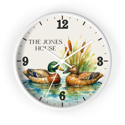 A round wall clock with a white frame and a printed watercolor-style design featuring two ducks on blue water with cattails and the text 'THE JONES HOUSE' on the clock face.