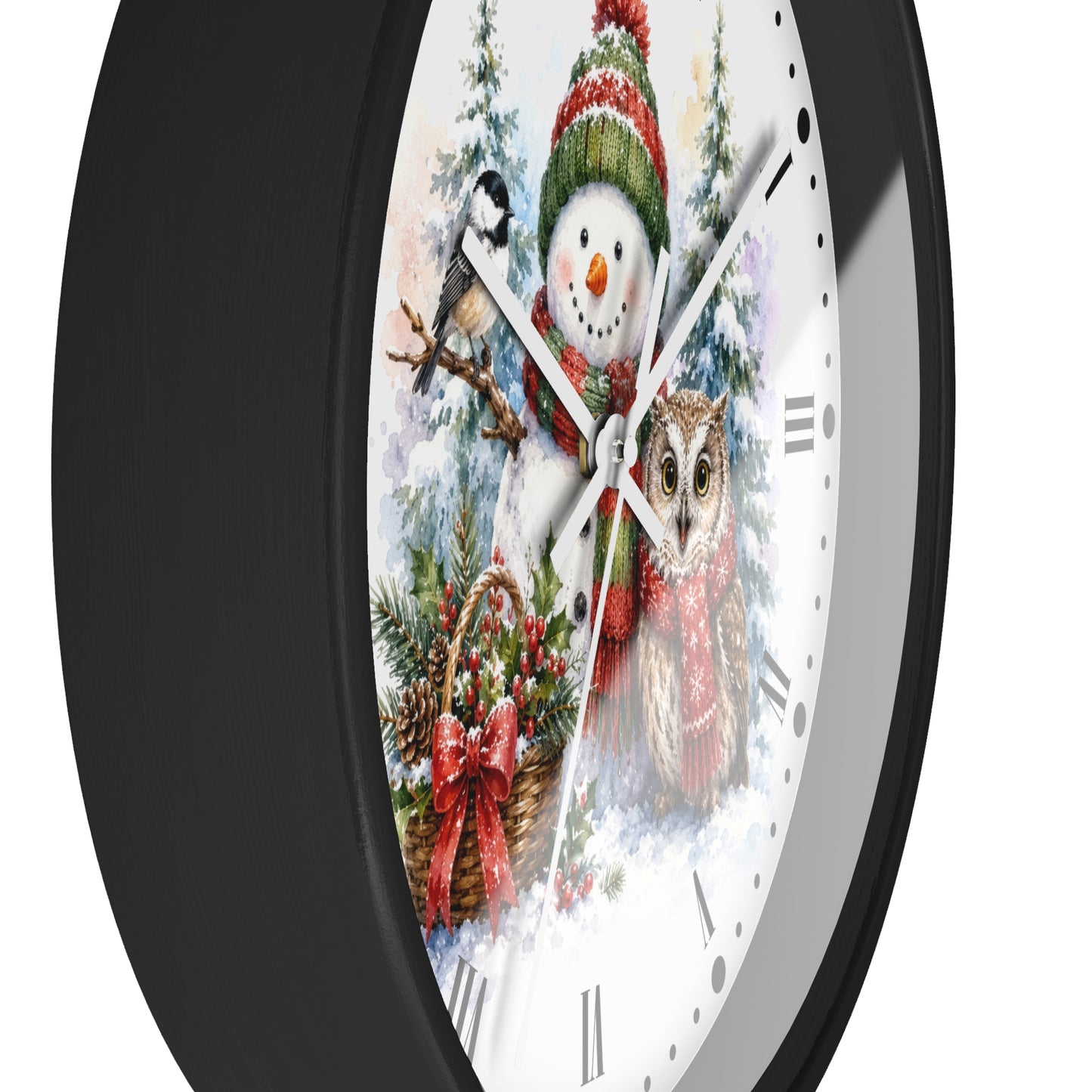 A round wall clock with a black frame and a white face featuring a festive winter illustration of a snowman, bird, owl, pine trees, and a basket with red bows.