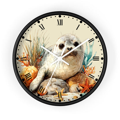 Round wall clock with a black frame and Roman numerals, featuring an illustrated seal sitting among rocks, shells, starfish, and seaweed on a light cream face.