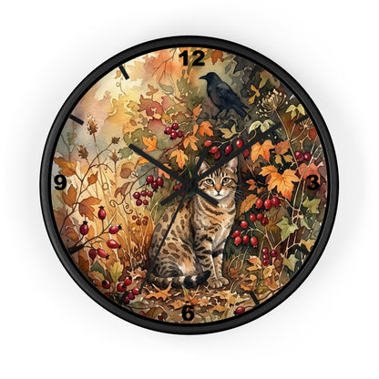 A round wall clock with a black frame and a detailed autumn-themed illustration on the face, featuring a tabby cat, a black bird, red berries, and orange and yellow leaves. The clock is shown against a plain white background.