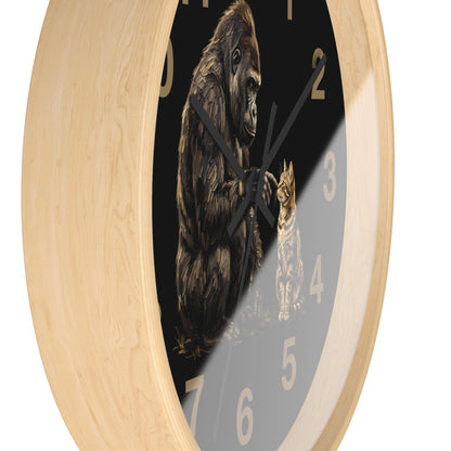 A round wall clock with a light natural wood frame and a black face featuring an illustration of a gorilla and a cat, with gold-colored numerals.