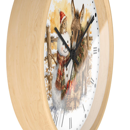 A round wall clock with a light natural wood frame and a white dial featuring a painted winter scene of a rabbit in a Santa hat next to a donkey, with black clock hands and Roman numerals.