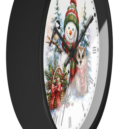 A round wall clock with a black frame and a white face featuring a festive winter illustration of a snowman, owl, bird, and holiday wreath.