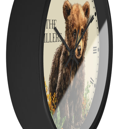 A round wall clock with a black frame and a printed face showing a brown bear illustration over a cream background with partial text and clock markers.