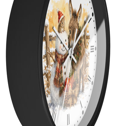 A round wall clock with a black frame and a white face featuring a winter illustration of a snowman and a donkey, shown against a plain white background.