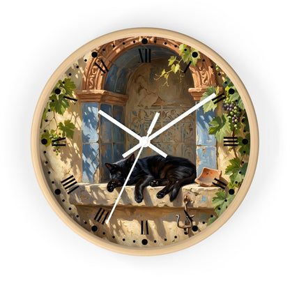 Round wall clock with a light wood frame and a printed illustration of a black cat sleeping on a stone windowsill beneath an arched window with blue shutters and climbing green vines. The clock face includes black Roman numerals and white hands, shown against a plain white background.