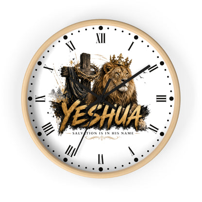 A round wall clock with a light wood frame and a white face featuring a lion wearing a crown, a wooden cross with chains, and the word 'YESHUA' in large gold letters. Roman numerals and black hands are visible on the clock.
