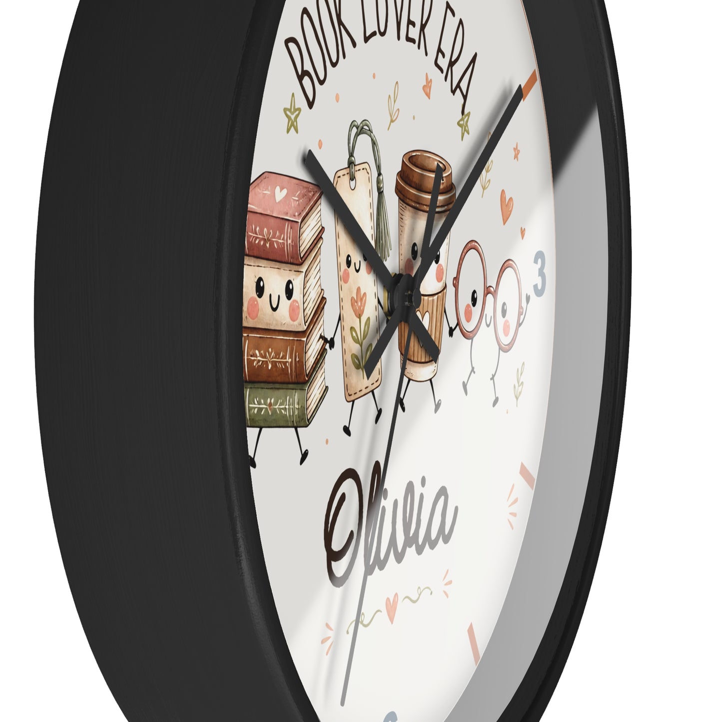 A round wall clock with a black frame and a white face featuring cute illustrations of books, a coffee cup, glasses, and the text 'BOOK LOVER ERA' and 'Olivia'.