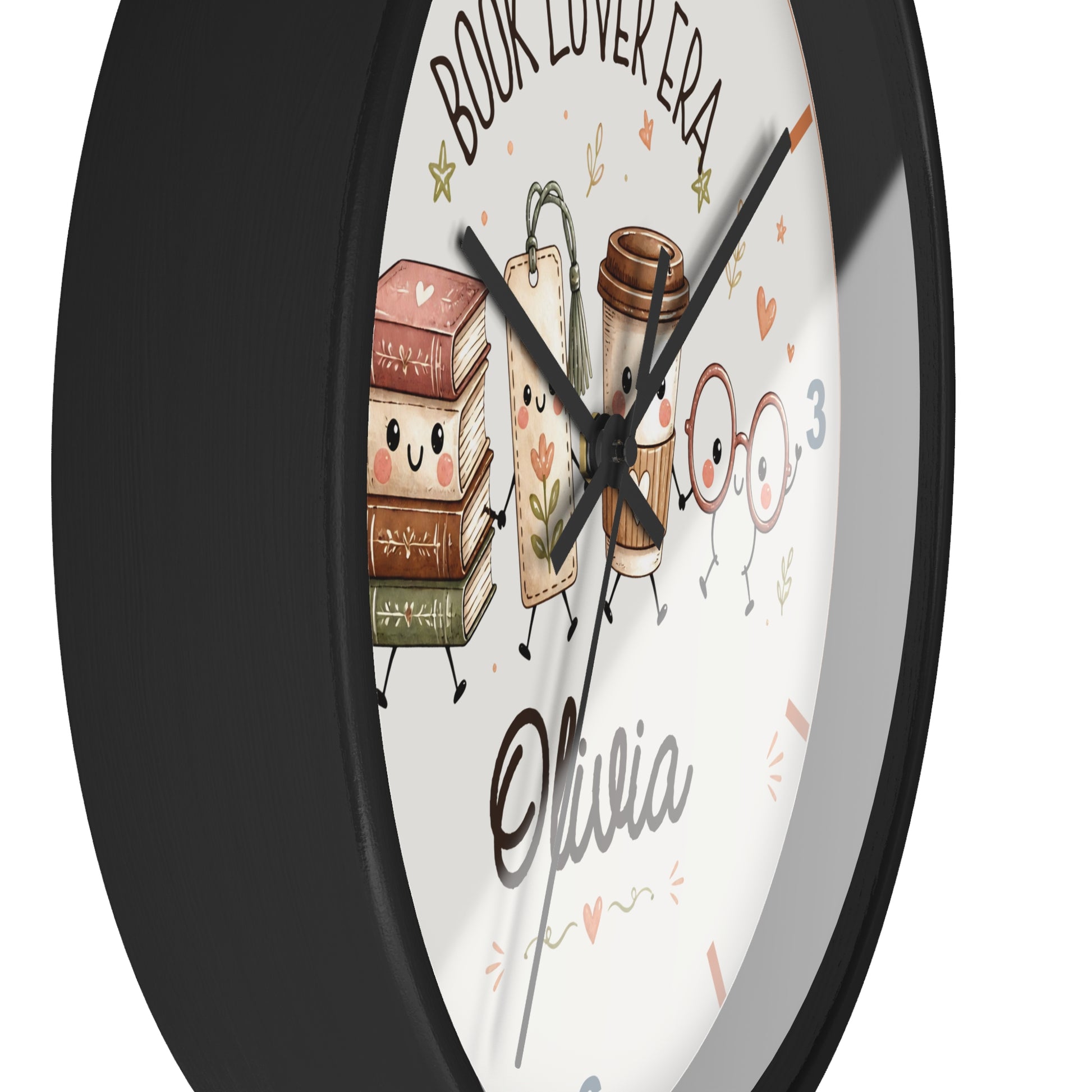 A round wall clock with a black frame and a white face featuring cute illustrations of books, a coffee cup, glasses, and the text 'BOOK LOVER ERA' and 'Olivia'.
