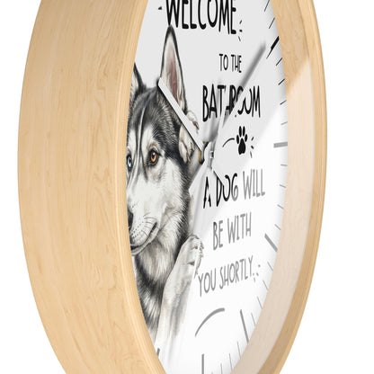 A round wall clock with a light natural wood frame and a white face featuring a detailed illustration of a husky dog and the text 'WELCOME TO THE BATROOM A DOG WILL BE WITH YOU SHORTLY'.