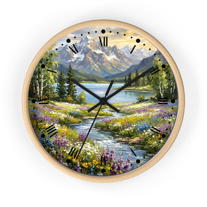 A round wall clock with a light wood frame and a scenic landscape print featuring mountains, a lake, trees, and a wildflower meadow. The clock face has black Roman numerals and black hands on a white background.