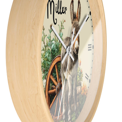 A round wall clock with a light natural wood frame and a printed face showing a donkey, a wagon wheel, flowers, and the name 'Miller' at the top.