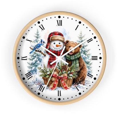 A round wall clock with a light wood frame and a white face featuring a festive winter illustration of a snowman in a red hat, a brown bear, snowy trees, and a blue bird, with black Roman numerals and white hands.