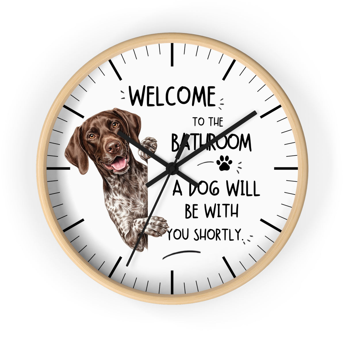 A round wall clock with a light wood frame and a white face, featuring a brown and white German Shorthaired Pointer dog illustration and the humorous text 'WELCOME TO THE BATHROOM A DOG WILL BE WITH YOU SHORTLY'.