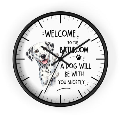 A round wall clock with a black frame and a white face featuring a Dalmatian illustration and the text 'WELCOME TO THE BATHROOM A DOG WILL BE WITH YOU SHORTLY.'.
