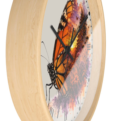 Round wall clock with a light natural wood frame and a printed butterfly artwork on the face. The design features a large orange and black butterfly over purple, pink, and orange watercolor-style floral splashes, with black clock hands and no visible numbers.