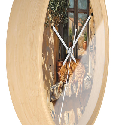 Round wall clock with a light natural wood frame and a printed scenic illustration of an orange tabby cat on a balcony, with white clock hands, shown on a white background.