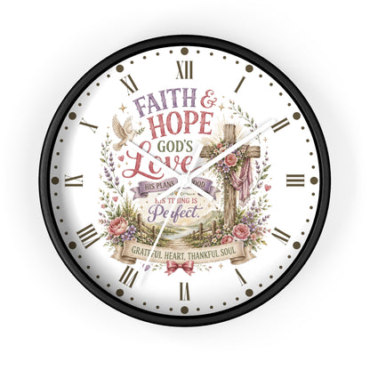 A round wall clock with a black frame and a white face featuring a Christian-themed floral and cross illustration with Roman numerals and the words 'Faith & Hope God's Love' and 'This Plan is Perfect.'.
