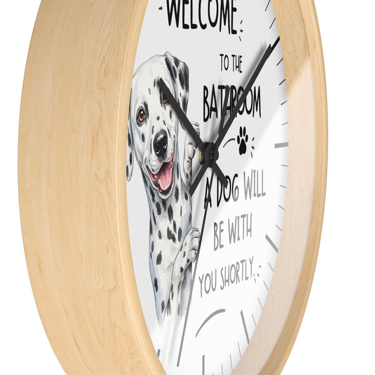 A round wall clock with a light natural wood frame and a white face featuring a Dalmatian illustration and the text 'WELCOME TO THE BATROOM A DOG WILL BE WITH YOU SHORTLY'.