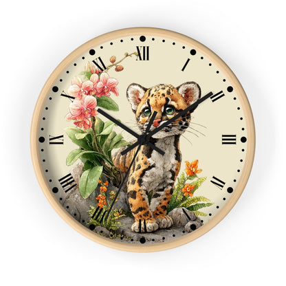 Round wall clock with a light wood frame and a cream-colored face, featuring a detailed illustration of a spotted kitten sitting among pink flowers and green leaves. The clock has black Roman numerals, black hands, and black minute markers.