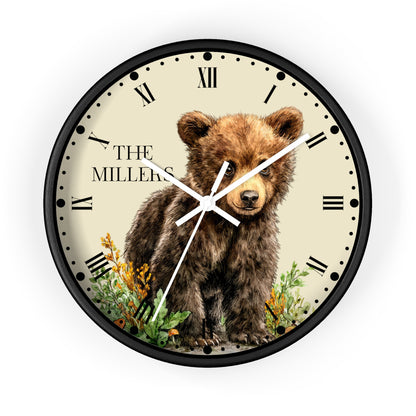 A round wall clock with a black frame and a cream-colored face featuring a brown bear illustration, Roman numerals, and the text 'THE MILLERS'.