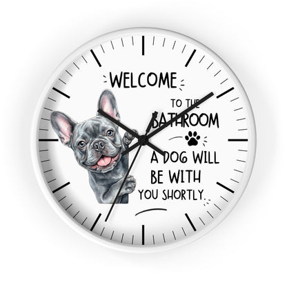 A round white wall clock with black hands and hour markers, featuring a French bulldog illustration and the text 'WELCOME TO THE BATHROOM A DOG WILL BE WITH YOU SHORTLY.' on a light gray background.