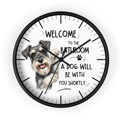 A round wall clock with a black frame and a white face, featuring a sketch of a gray and white terrier dog and the text 'WELCOME TO THE BATHROOM A DOG WILL BE WITH YOU SHORTLY.' on a light gray background.