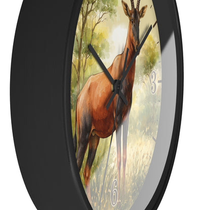 Round wall clock with a black frame and a printed illustration of a brown antelope standing in a sunlit grassy landscape. The clock face is partially visible behind the frame, with black hands and partial gray numerals, shown against a white background.