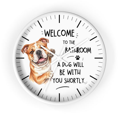 A round white wall clock with black hands and hour markers, featuring a brown and white bulldog illustration on the left and the text 'WELCOME TO THE BATHROOM A DOG WILL BE WITH YOU SHORTLY.' on a white background.