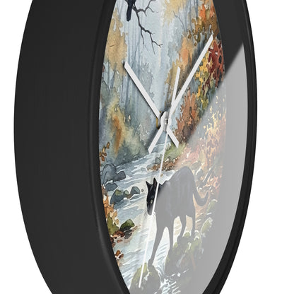 Round wall clock with a black frame and a printed autumn forest scene featuring a black cat walking near a stream. The clock is shown at an angle against a plain white background.