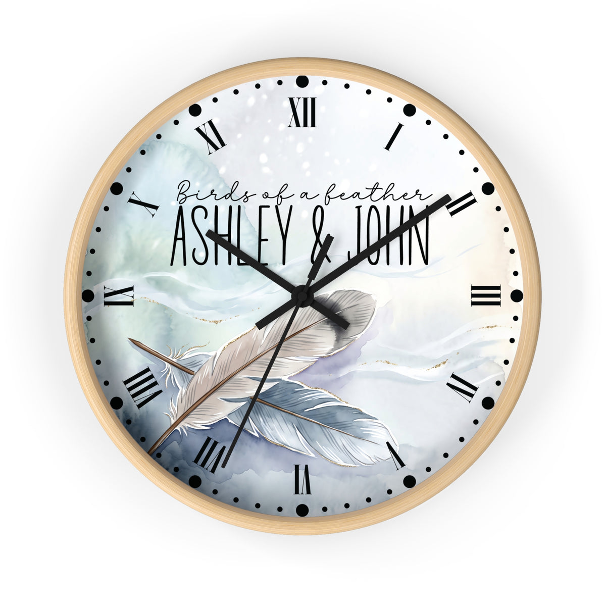 A round wall clock with a light wood frame and a printed dial featuring the text 'Birds of a feather ASHLEY & JOHN' over an illustration of two feathers on a soft blue and white background.