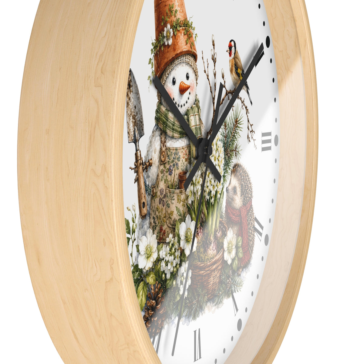 A round wall clock with a light natural wood frame and a white face featuring a whimsical winter garden illustration. The design shows a snowman wearing a terracotta flower pot hat and green scarf, holding a trowel, with a small bird perched on the clock hands and Roman numeral hour markers.