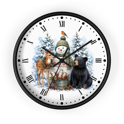 A round wall clock with a black frame and a white face featuring a winter holiday illustration. The design shows a snowman in a green hat, a deer with a wreath, a black bear, snow trees, and a small bird, with black Roman numerals and hands on a white background.