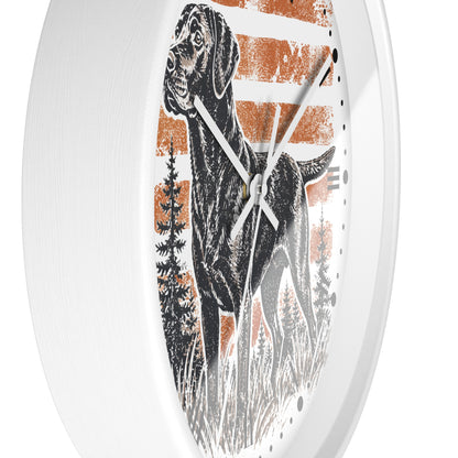 An oval wall clock with a white frame and a printed design featuring a black dog standing in front of distressed orange and white horizontal stripes, with dark trees at the bottom.