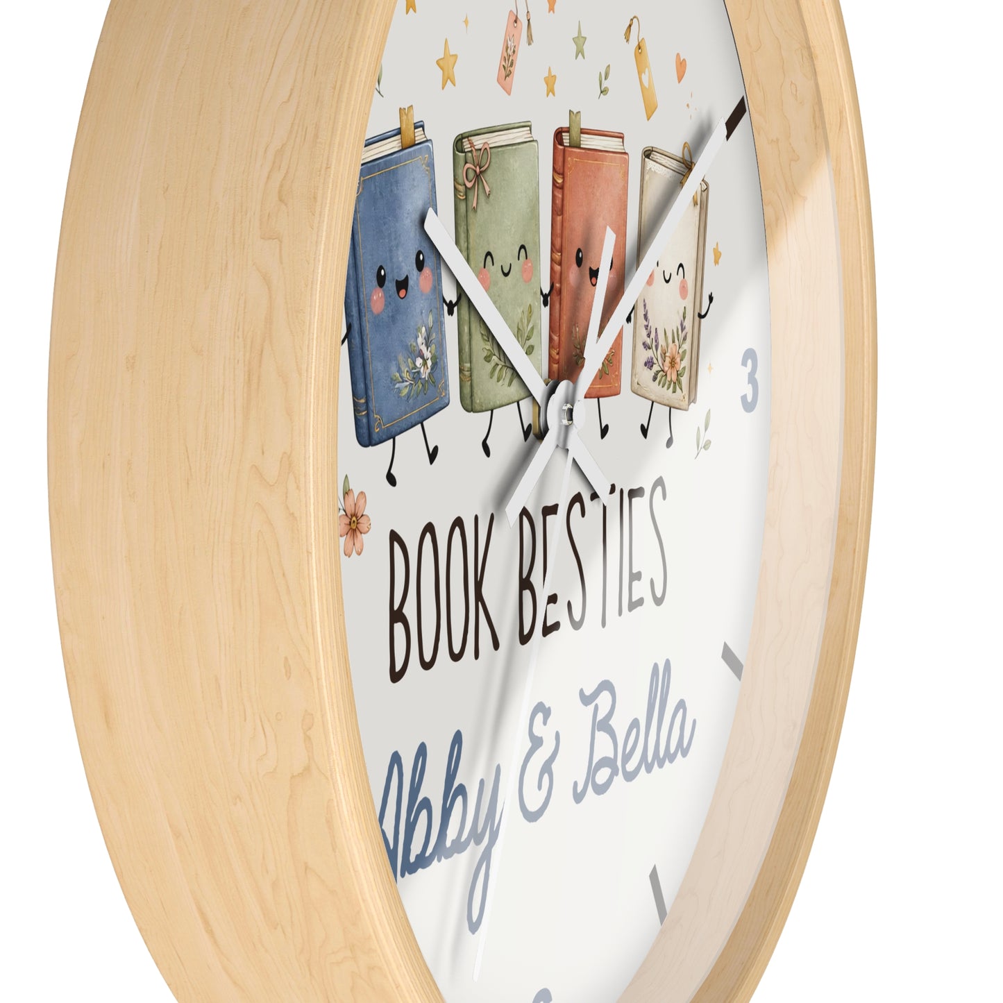 A round wall clock with a light natural wood frame and a white face featuring four cute illustrated books with faces and arms, plus the text 'BOOK BESTIES' and 'Abby & Bella'.