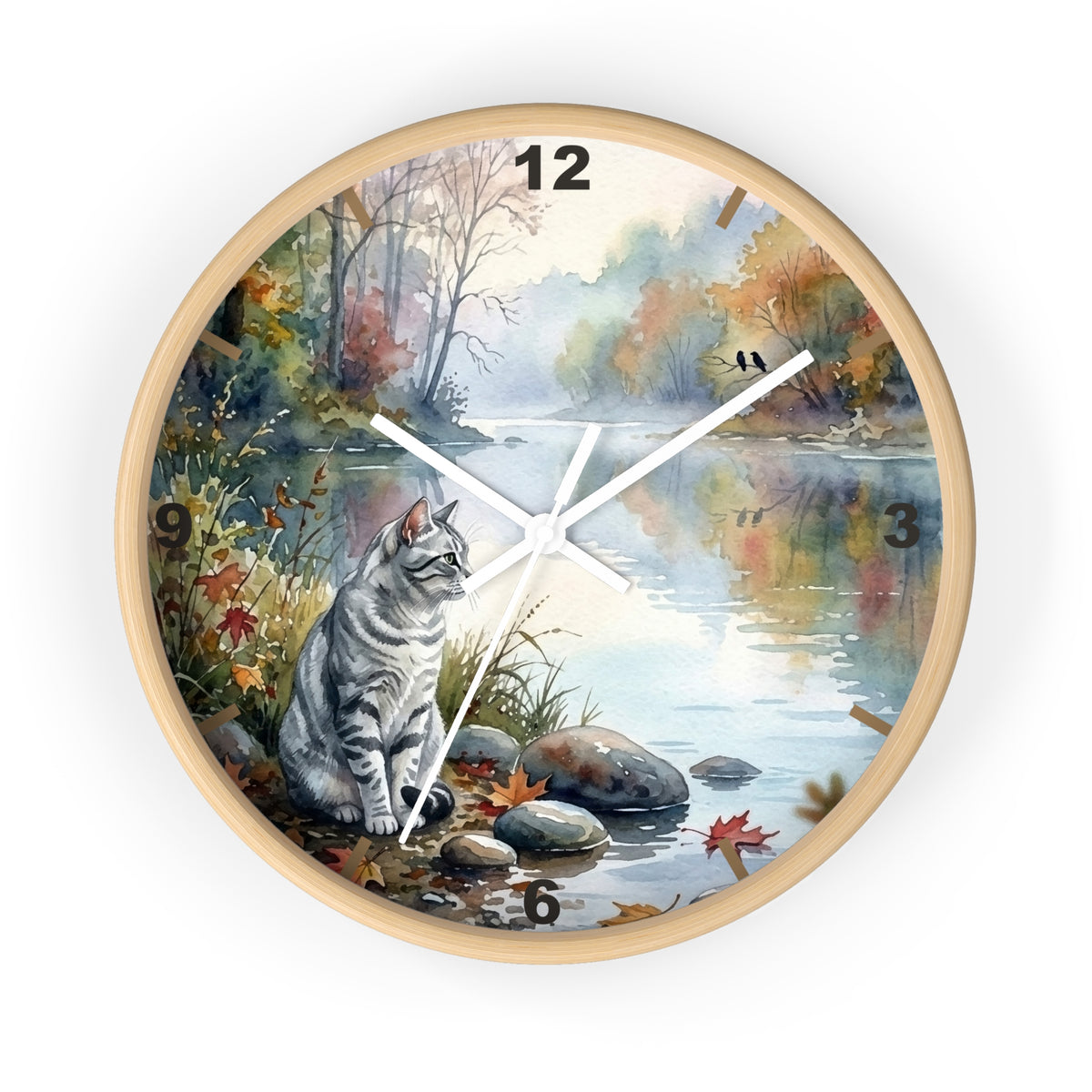 Round wall clock with a light wood frame and a printed scenic dial showing a gray tabby cat sitting by a river in an autumn landscape. The clock has black numerals and white hands on a white background.
